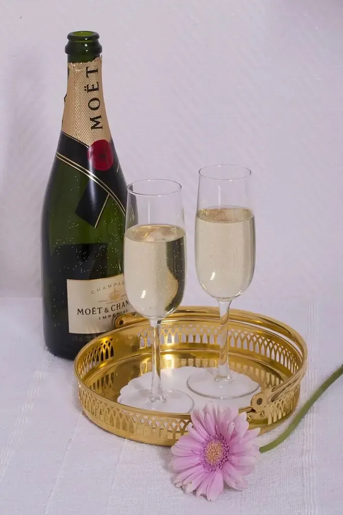 Champagneflaska och två fyllda glas på en mässingsbricka med en rosa blomma.