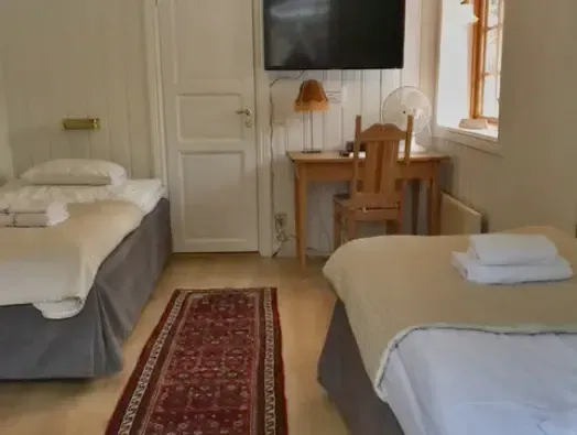 Tvåbäddsrum med bäddade sängar, skrivbord och tv på väggen.